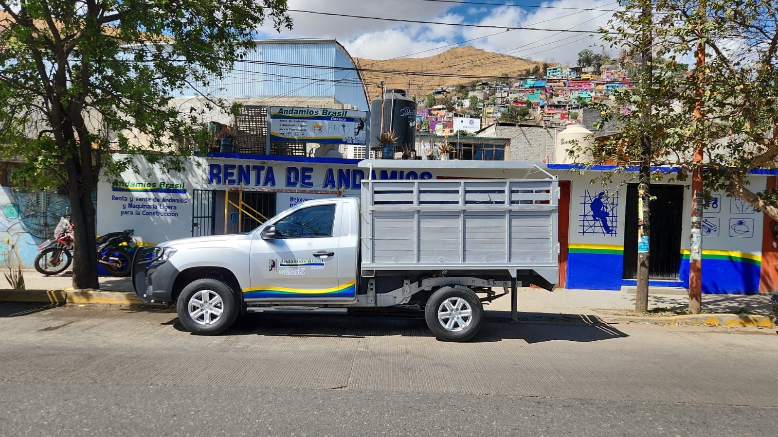 Camioneta blanca estacionada en la calle frente a un colorido edificio con una montaña de fondo.