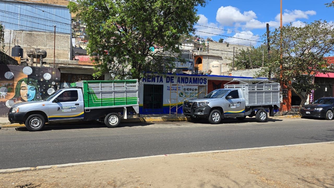 Dos camiones de trabajo estacionados frente a un edificio con las palabras 