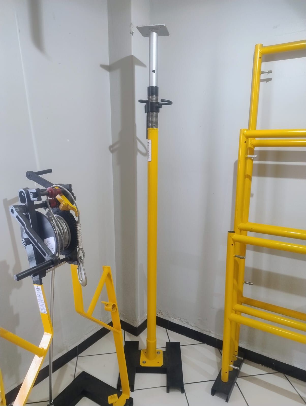 Equipos de construcción amarillos: andamios, pértiga ajustable y carrete de cable, en interiores.