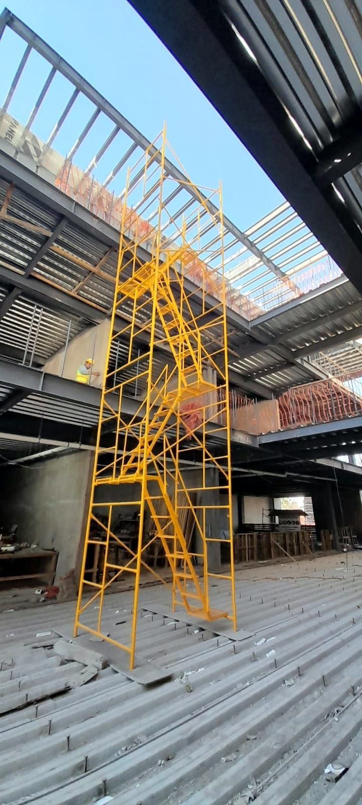 Andamios amarillos sobre techo de chapa ondulada bajo un tejado con estructura metálica.
