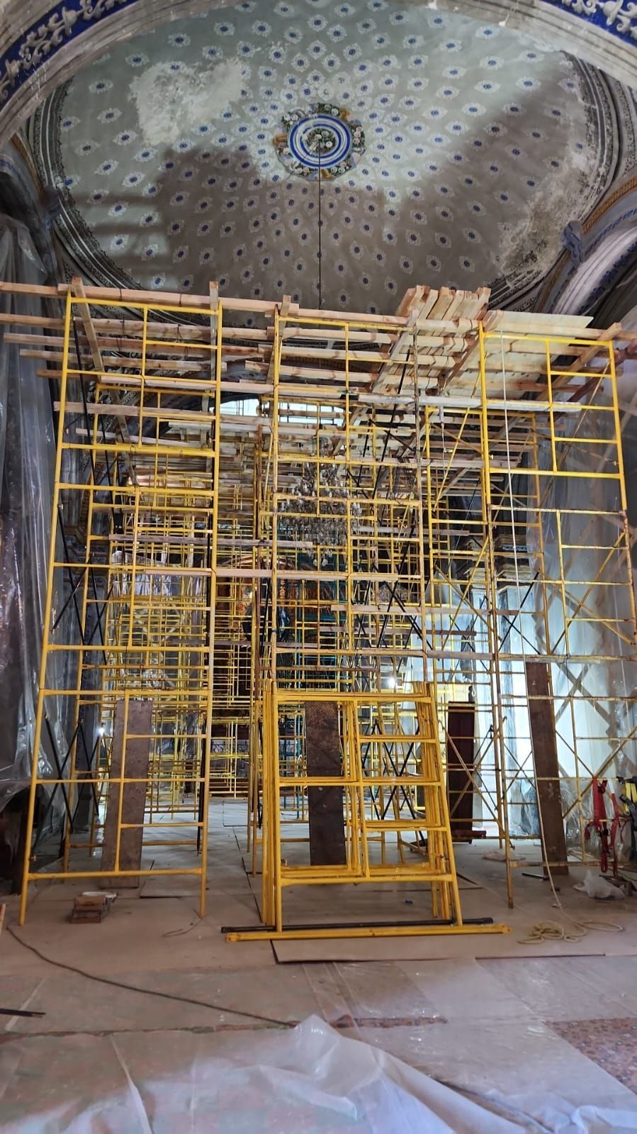 Andamios instalados en el interior de un edificio con techo decorado; obras en curso.