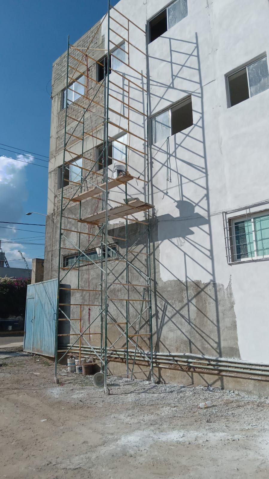 Andamios en un edificio en construcción, vista exterior, con ventanas y paredes de color claro, día soleado.