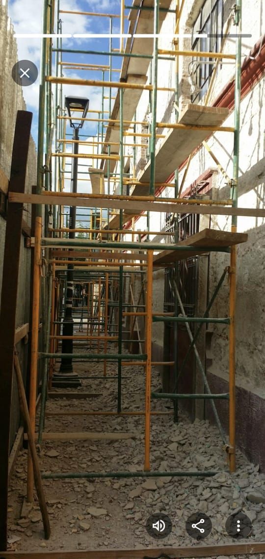 Andamios entre edificios, obra en construcción. Vista de un estrecho pasadizo con escombros en el suelo.