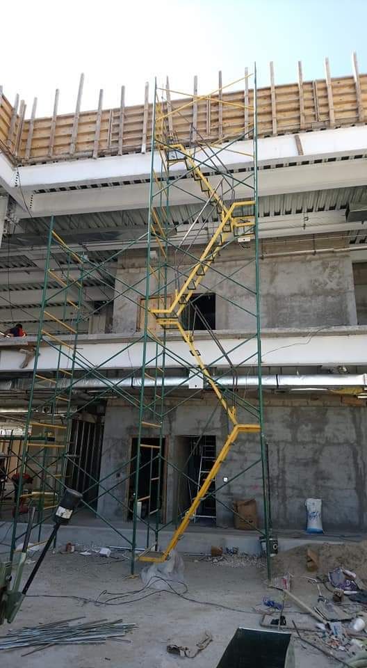 Andamios en una obra en construcción, escalera amarilla alta, edificio de hormigón.