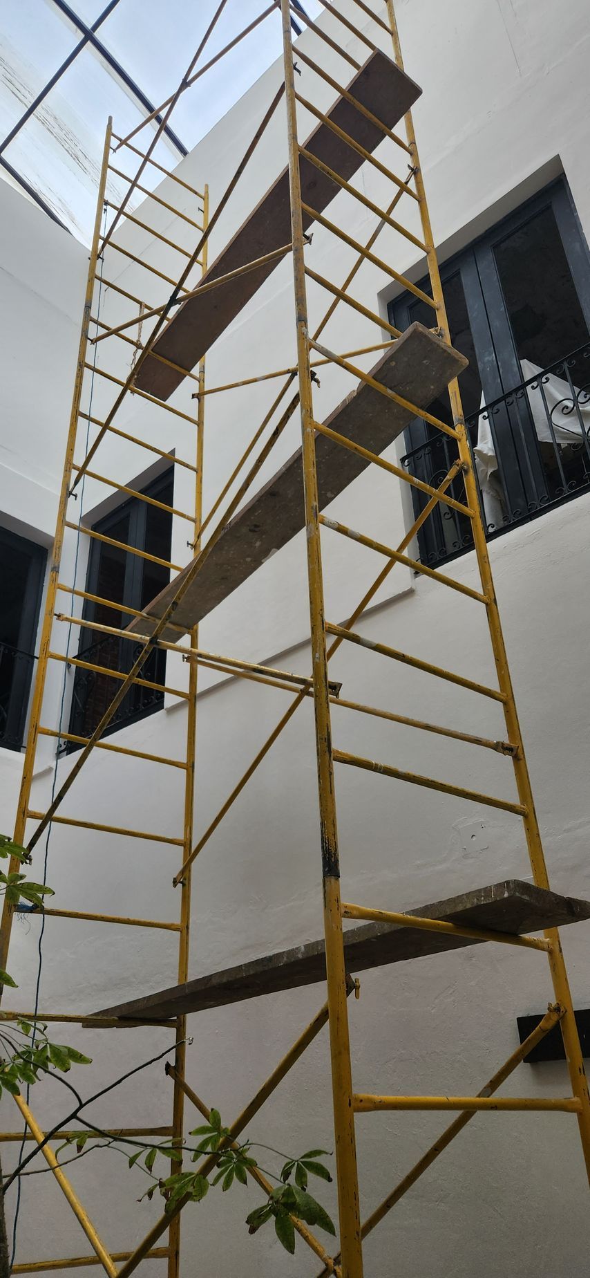Un alto andamio amarillo con tablones adheridos se alza contra un edificio blanco con ventanas.