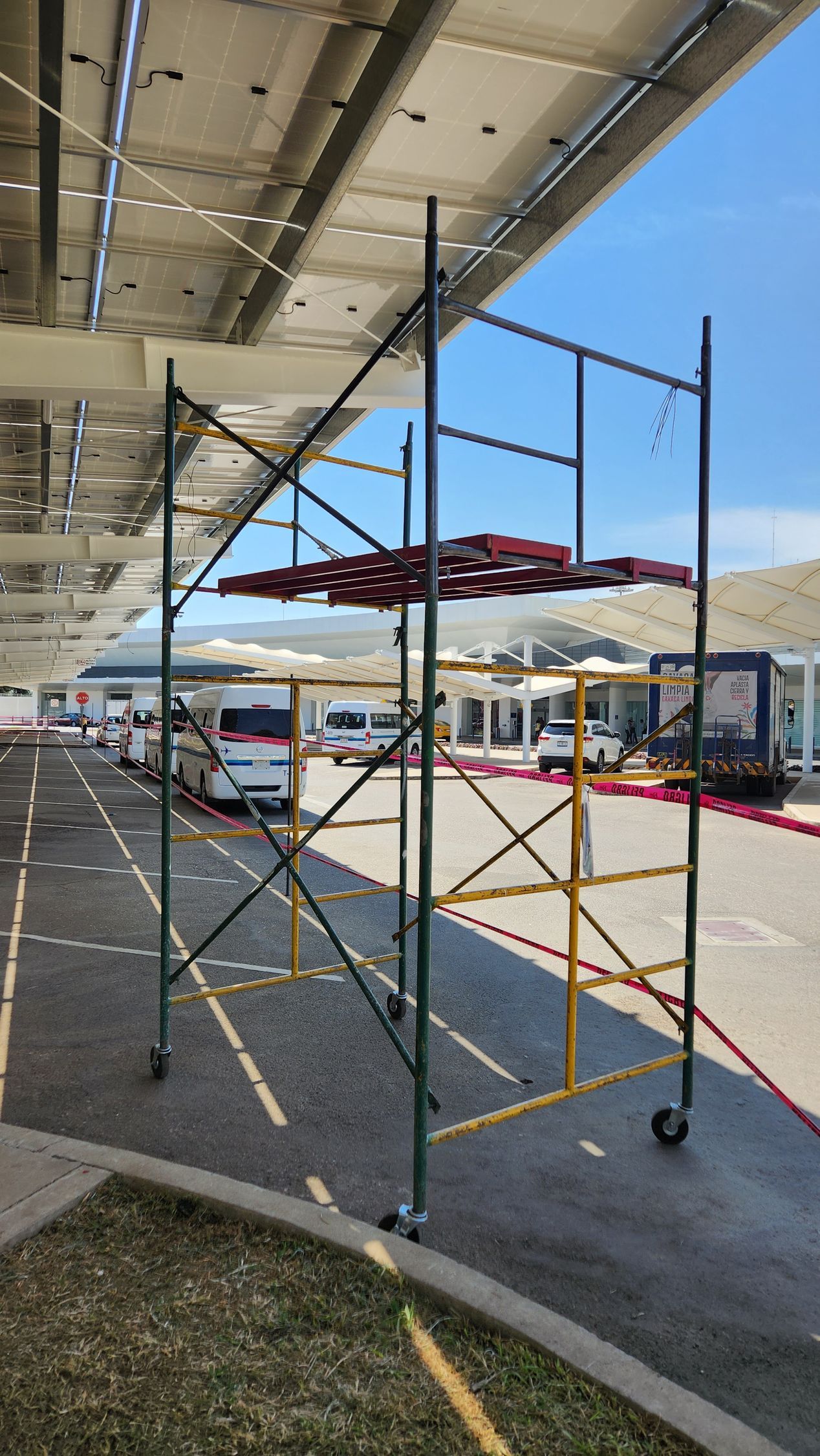 Andamios con materiales rojos en la parte superior cerca de la entrada de un edificio bajo un techo de paneles solares.