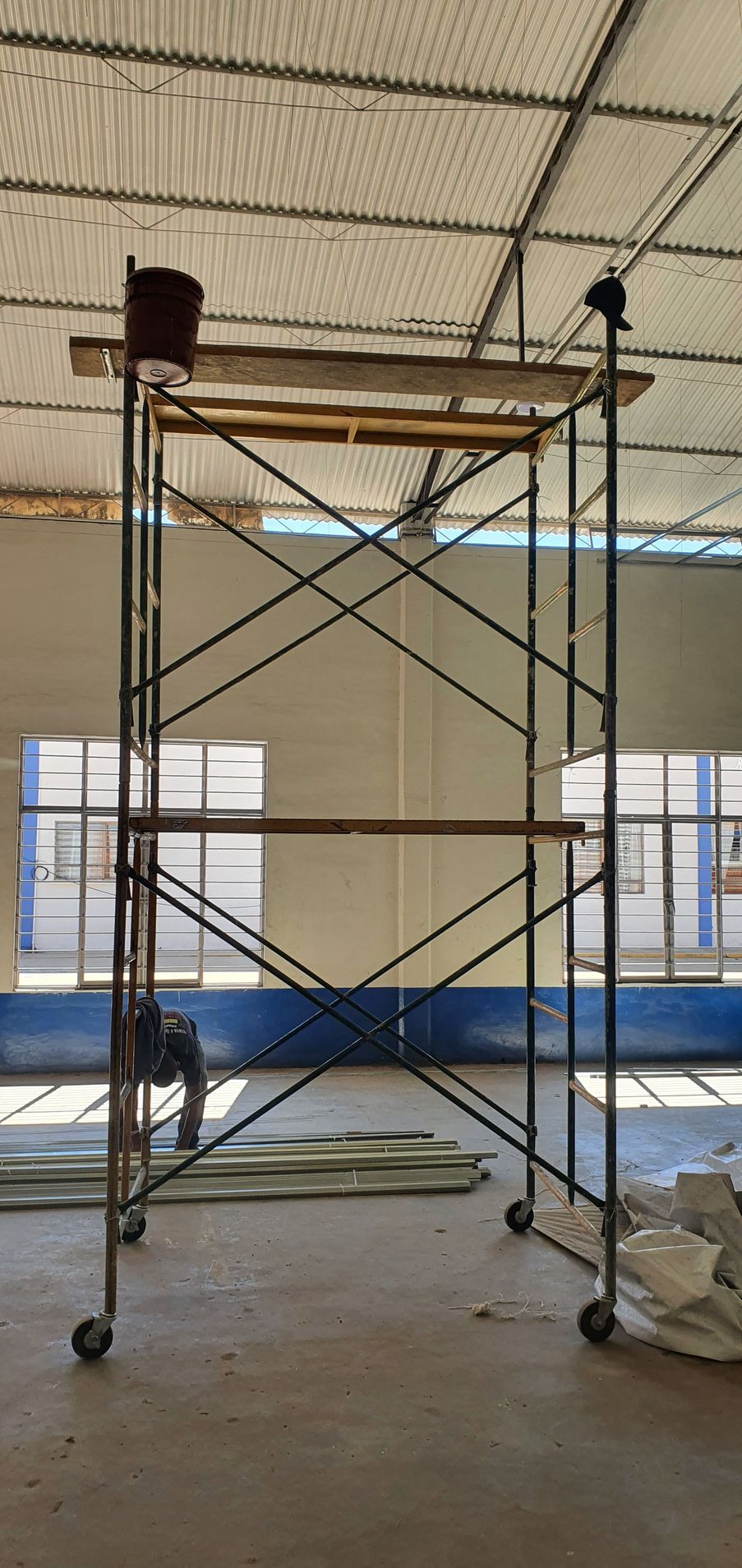 Un andamio metálico sobre ruedas en un edificio industrial. Se puede ver a una persona cerca de la base.