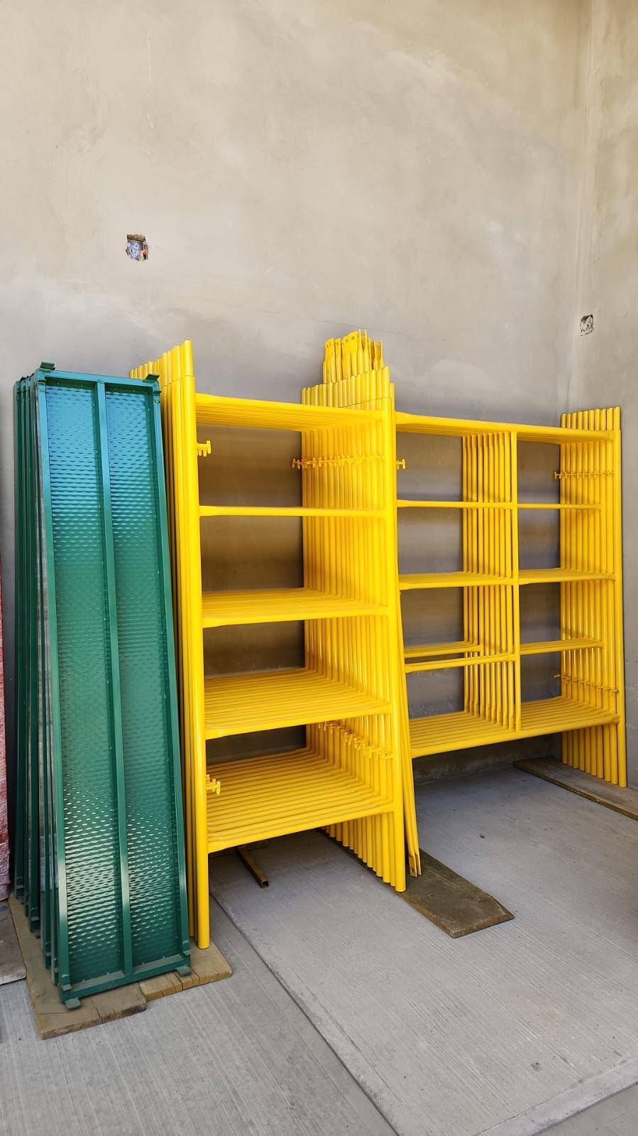 Andamios metálicos amarillos apilados con paneles metálicos verdes contra una pared color canela.