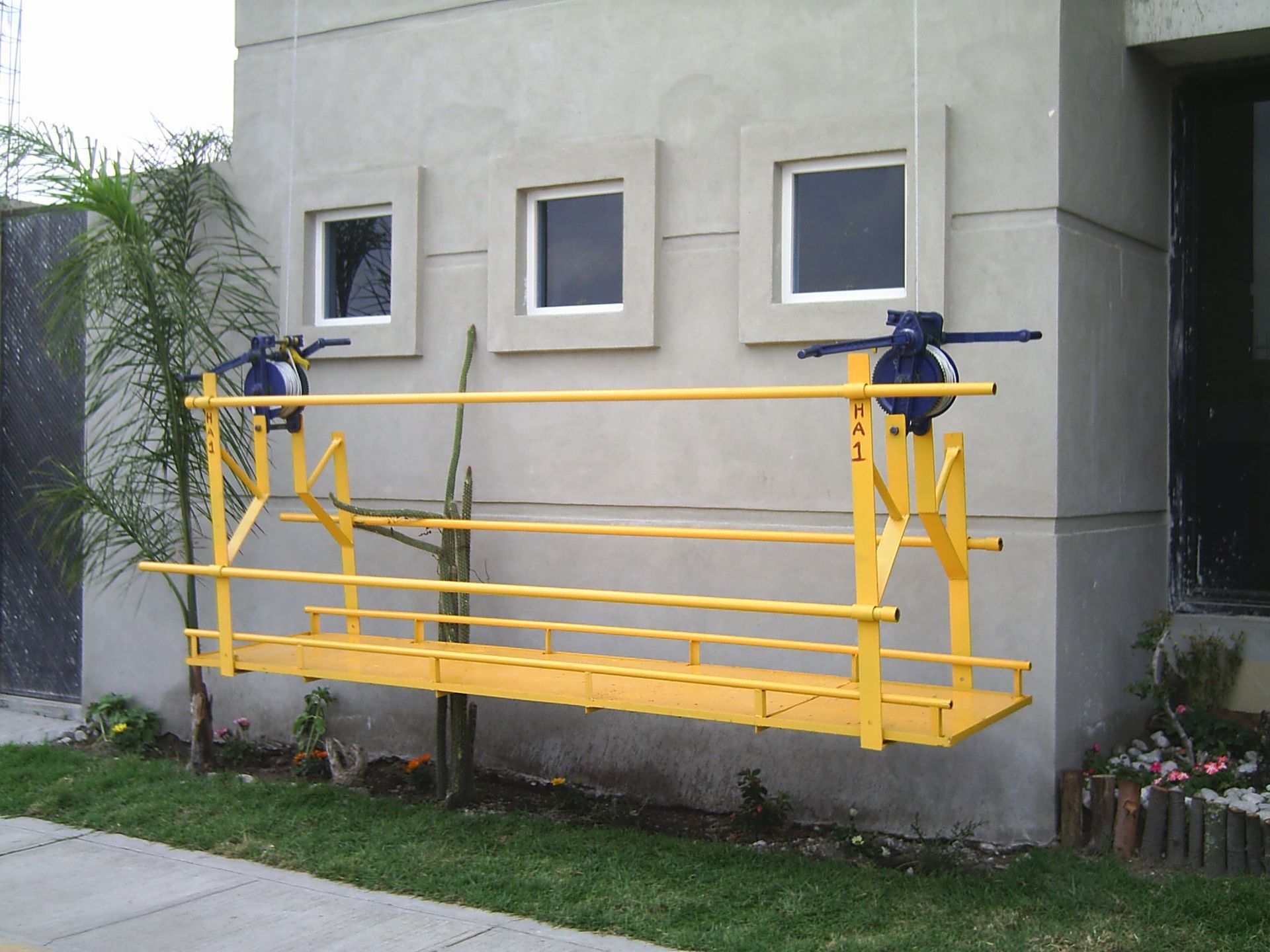 Andamio suspendido amarillo en el exterior de un edificio con tres ventanas.