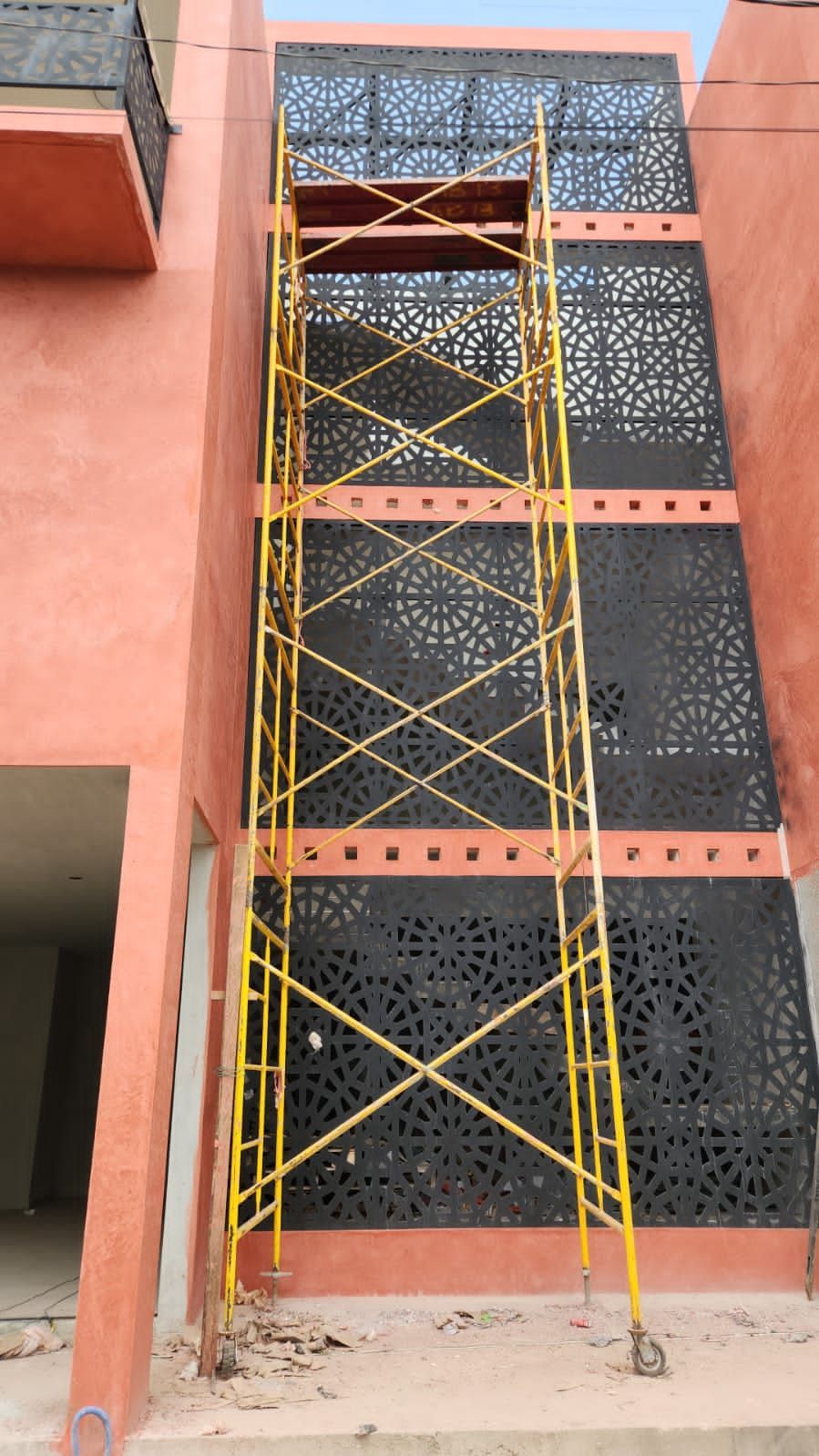 Andamios adosados ​​a la fachada de un edificio con recortes decorativos. La estructura es de color melocotón, con paneles negros y andamios amarillos.