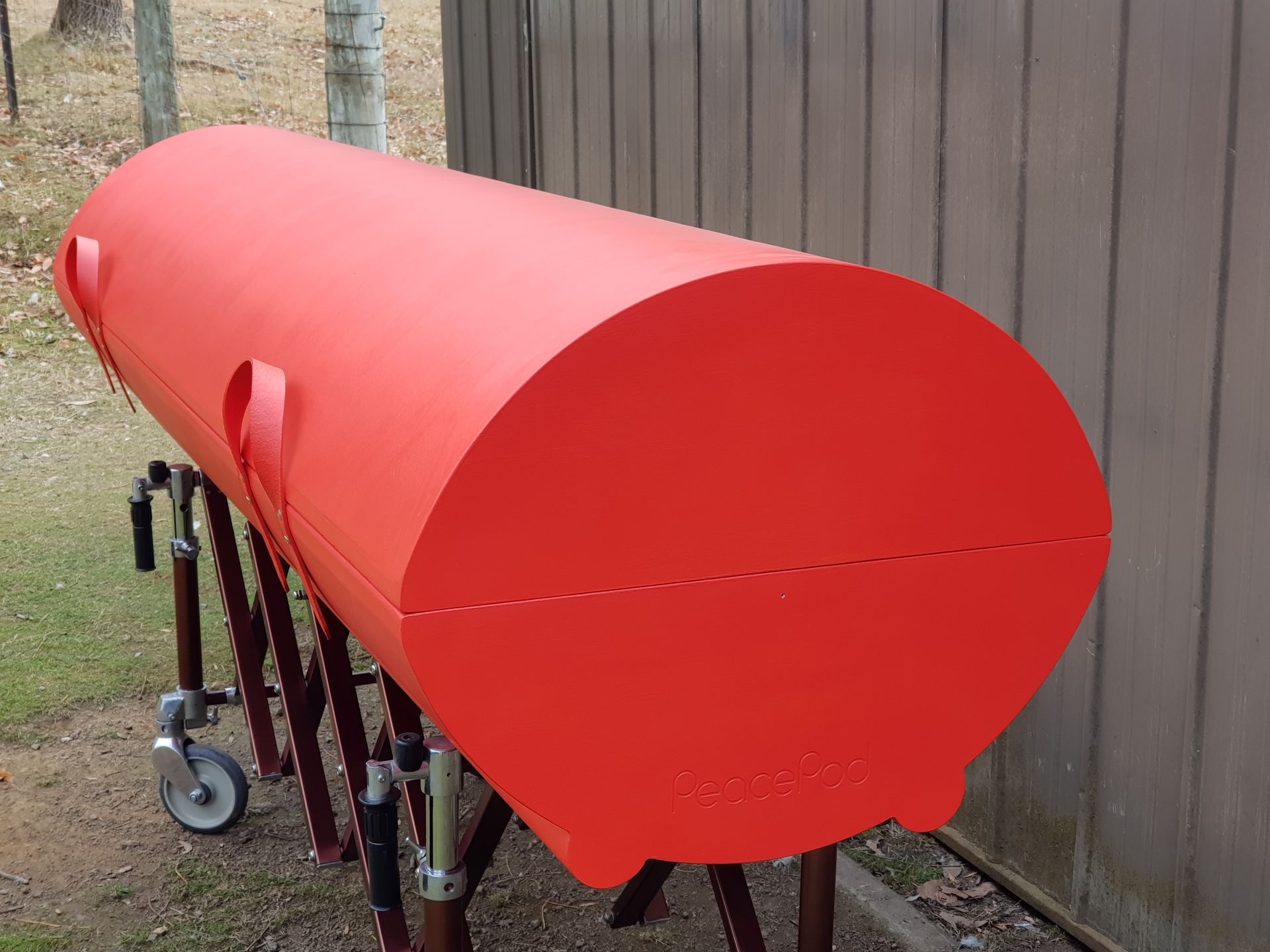 A large red coffin is sitting on a stand next to a rural fire brigade shed