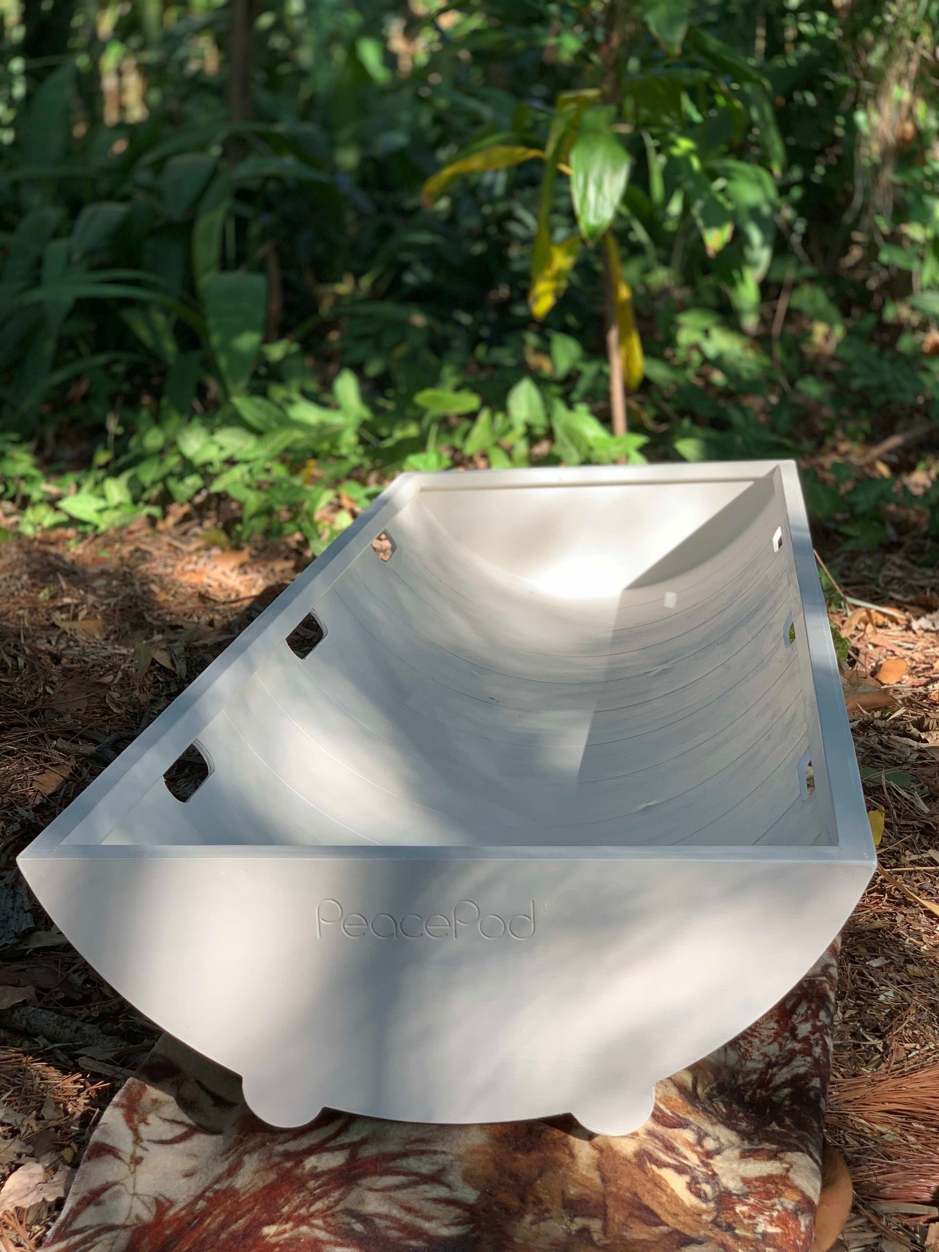 A white shroud bearer tray is sitting on top of a pile of leaves in the woods.
