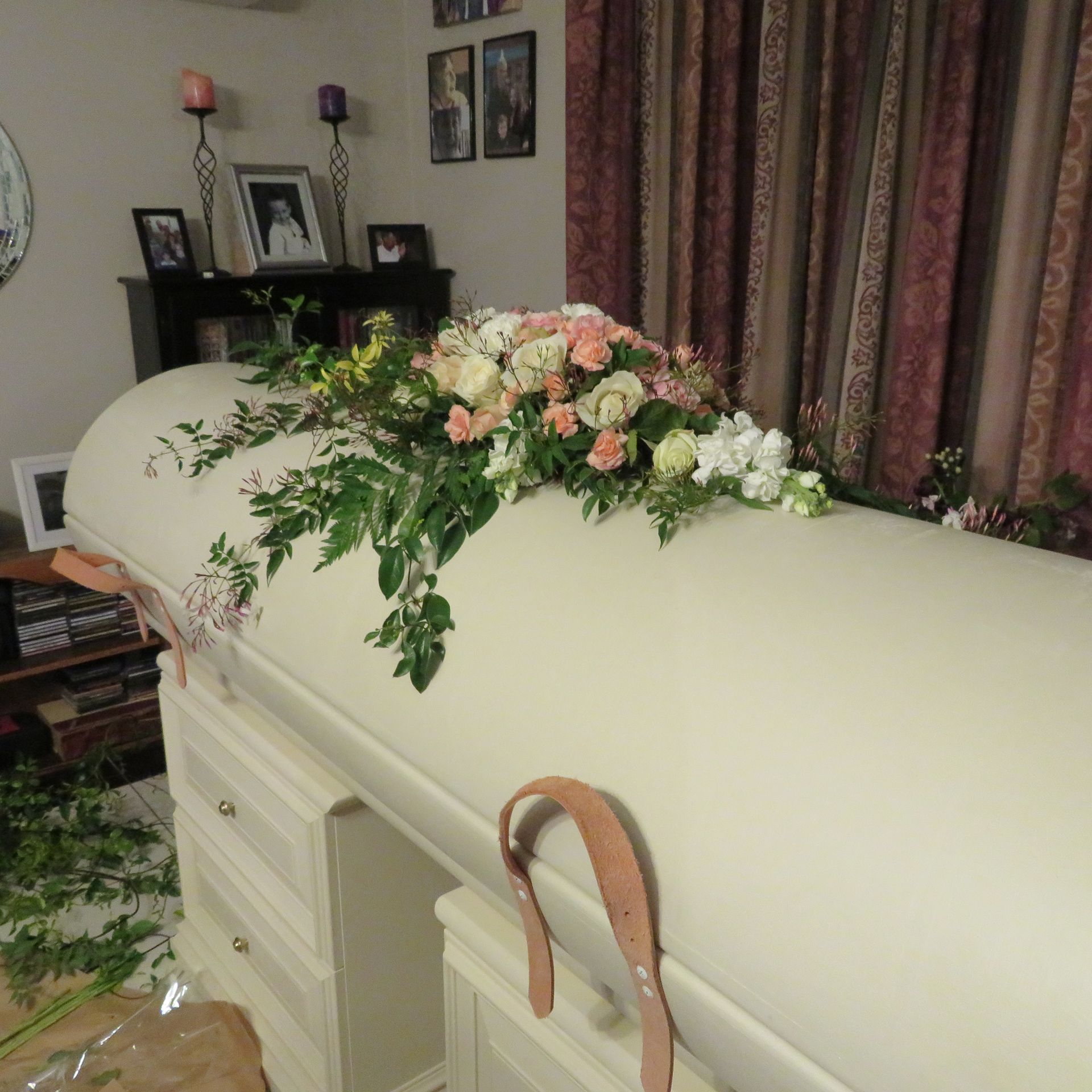 A white coffin is decorated with flowers in a living room