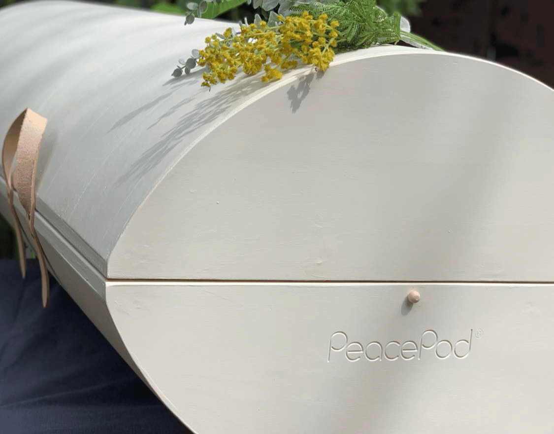 A white coffin with flowers on top of it is sitting on a table.