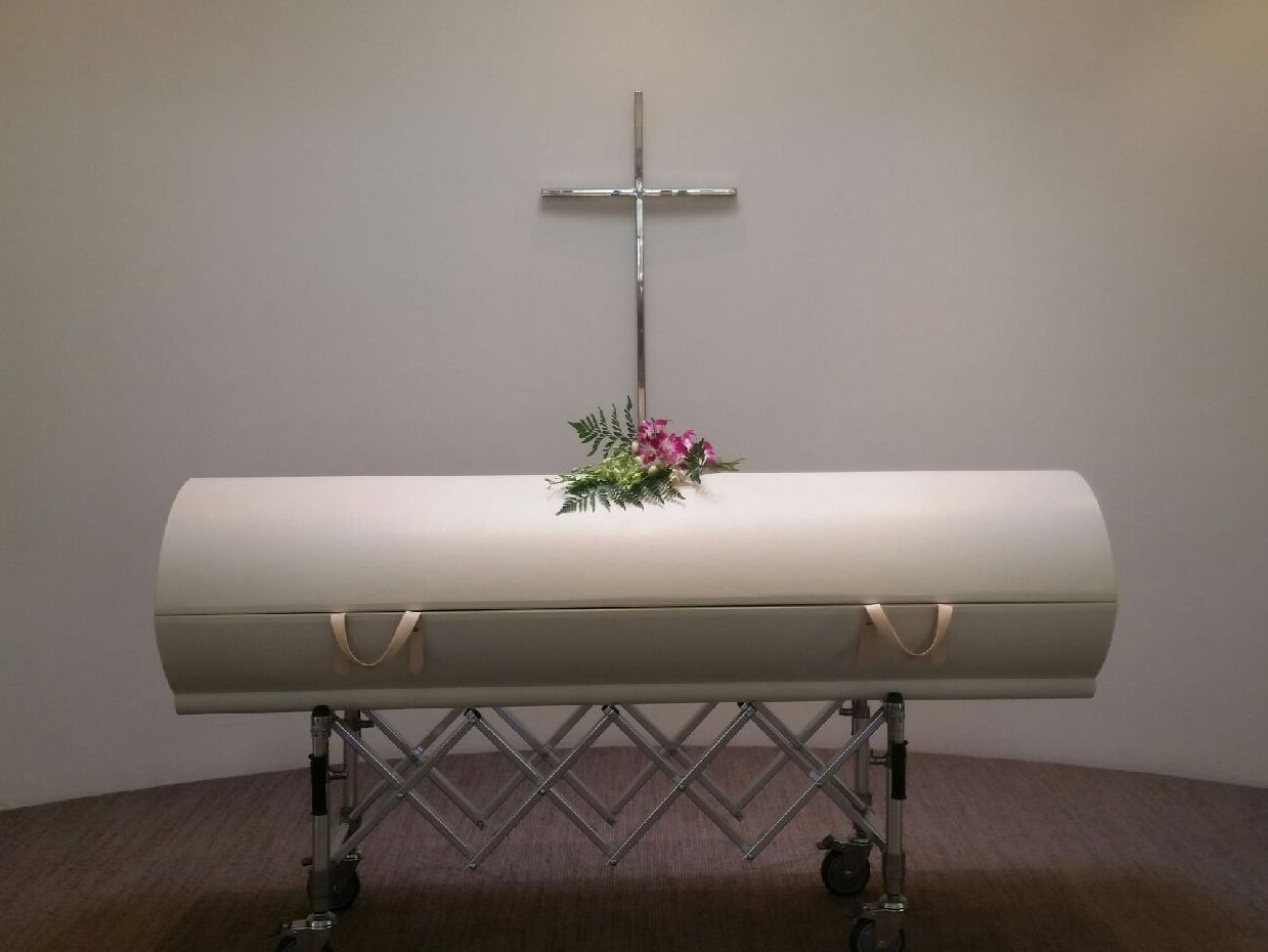 A white coffin with a cross in the background