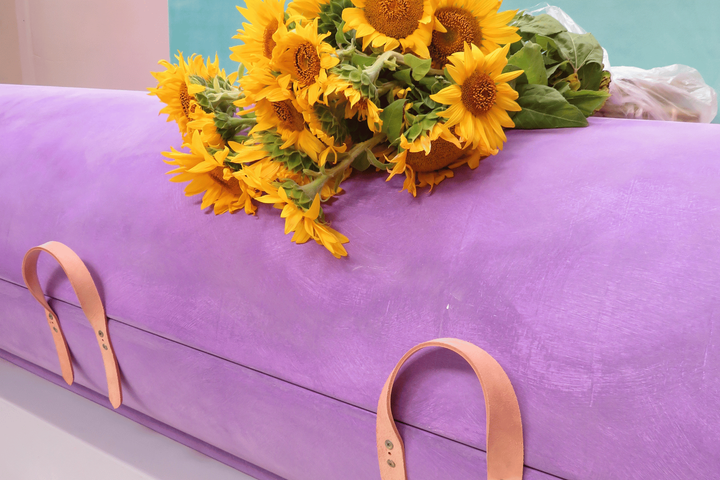 A purple coffin with sunflowers on top of it.
