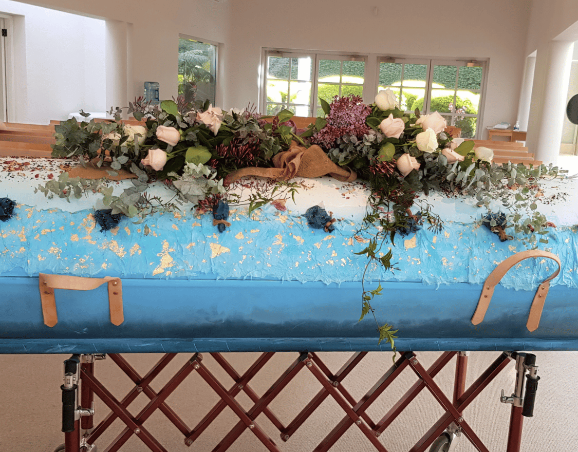 A blue coffin with flowers on it is sitting in a room.