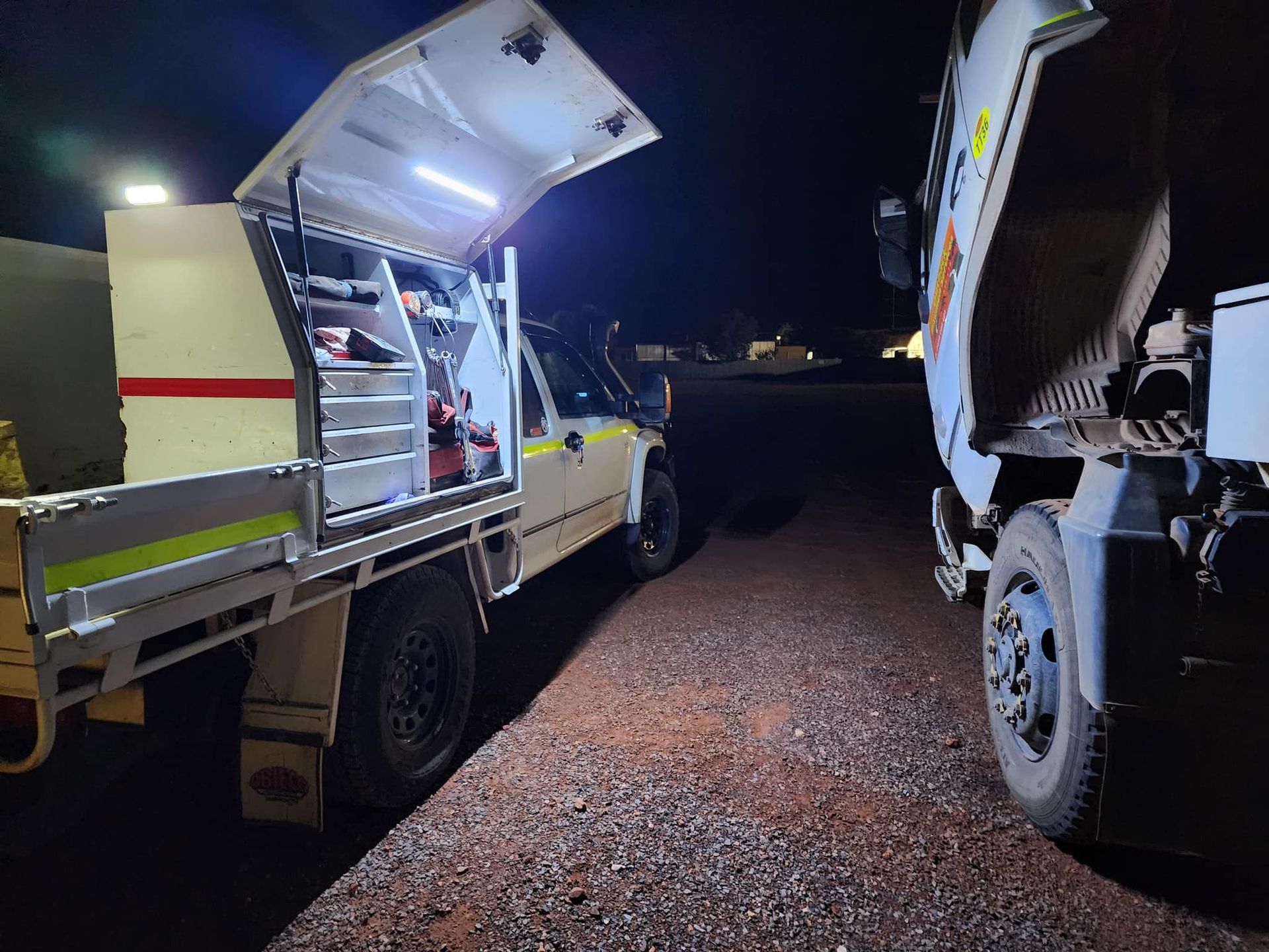 A work truck with open canopy lit up at night, next to another truck.