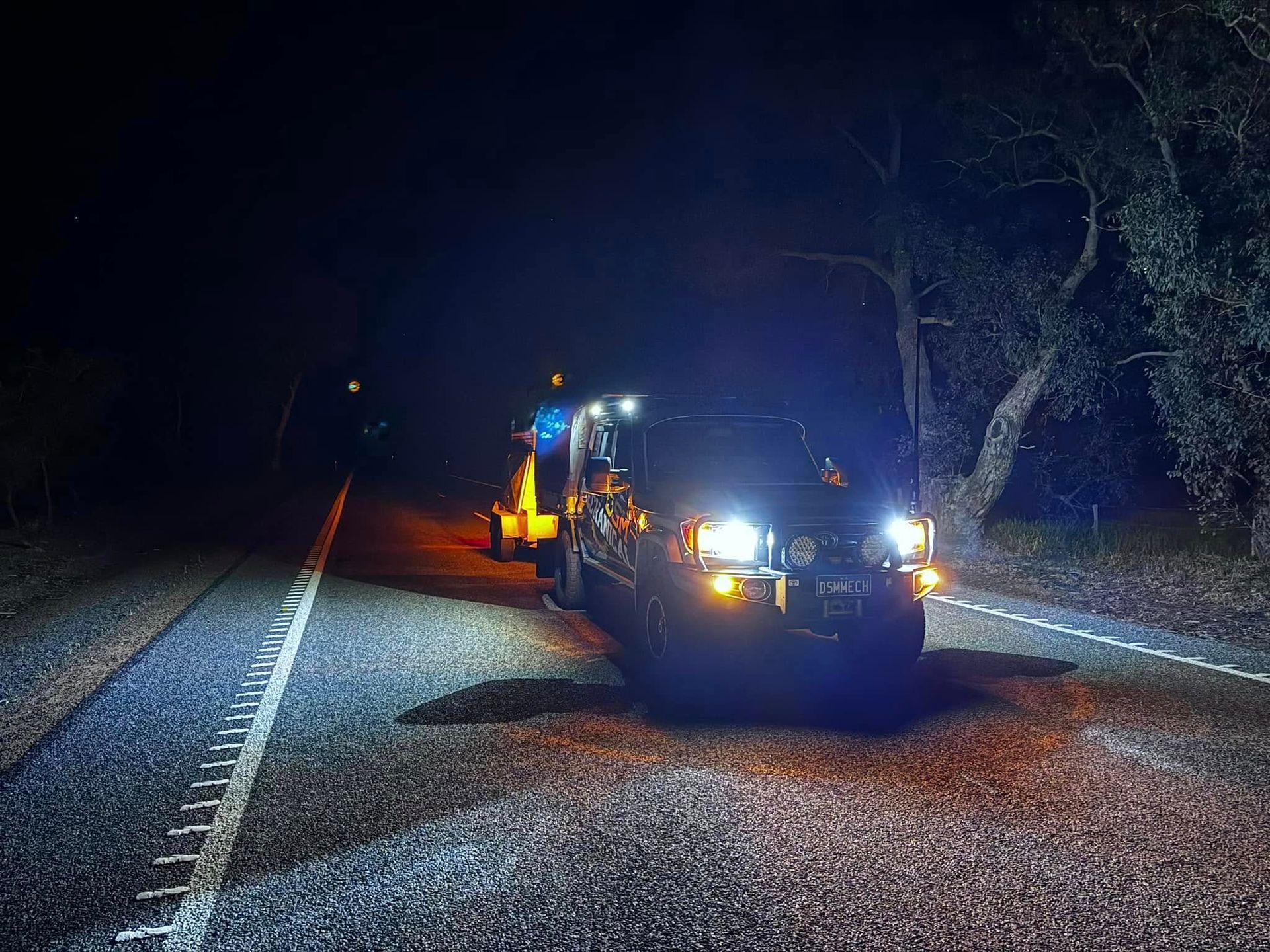 Truck with lights on, towing equipment, parked on a road at night.