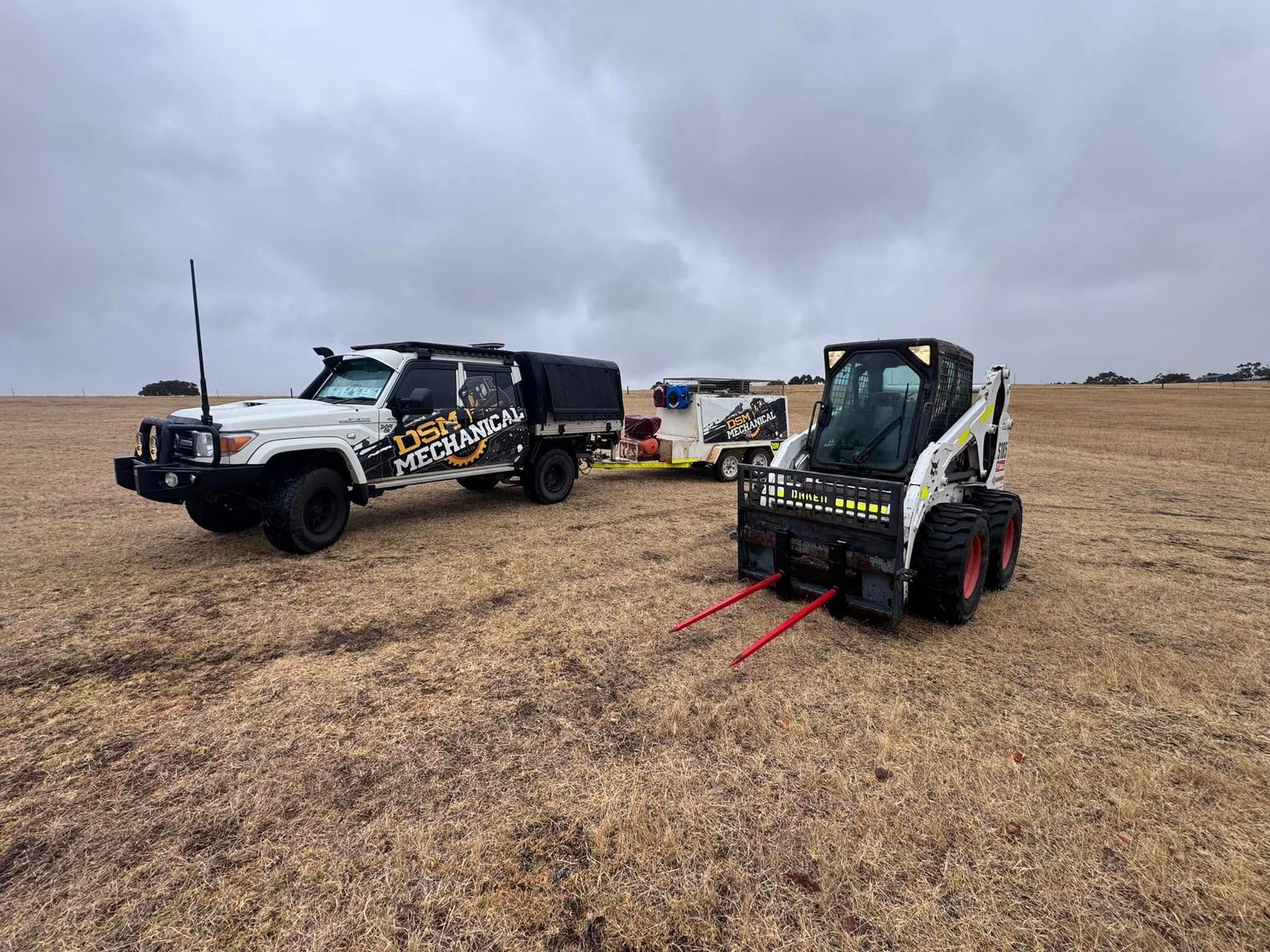 White truck with trailer and Bobcat in a field. Cloudy sky.