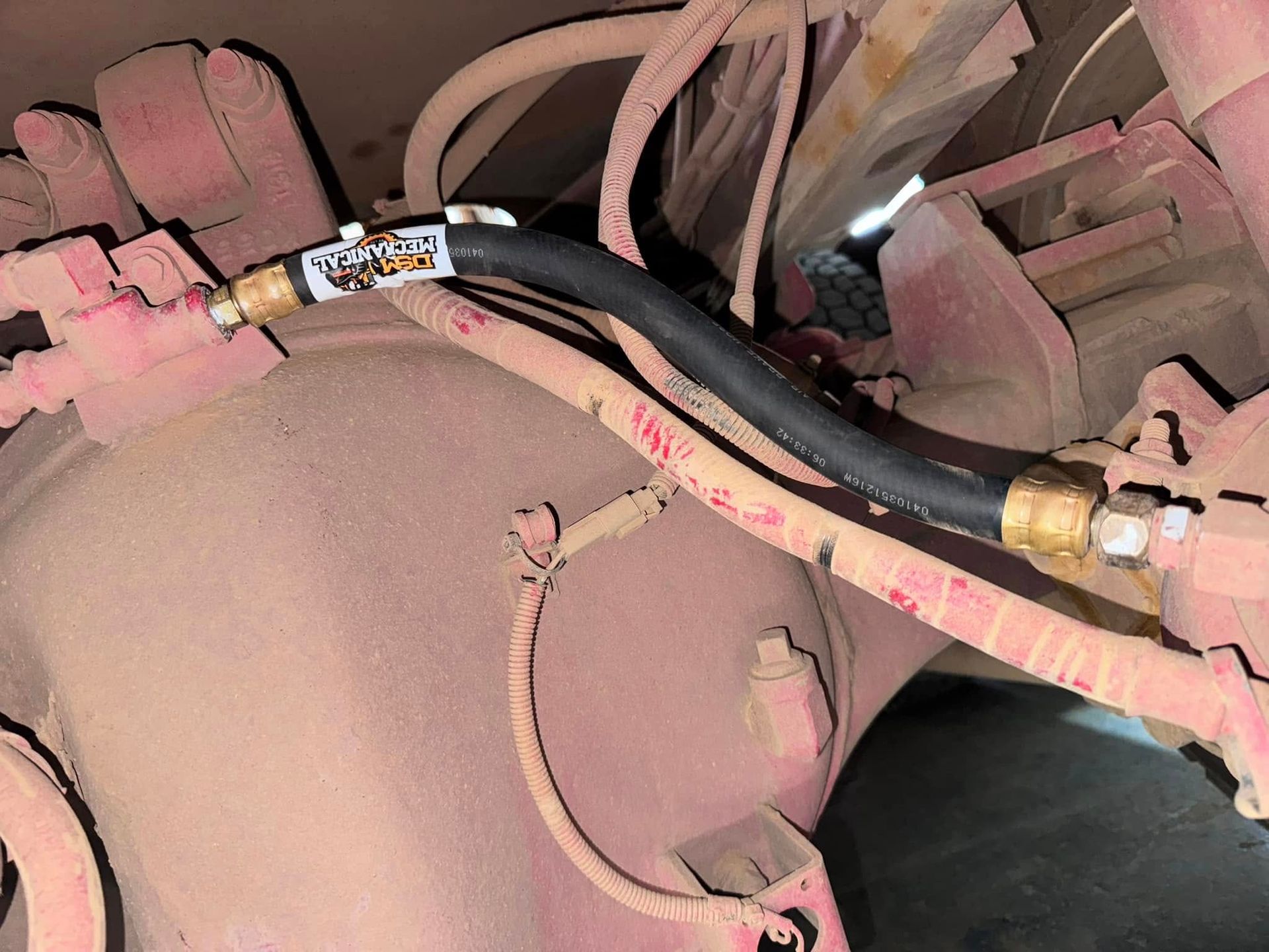 Black hose with brass fittings connected to a dusty vehicle component, labeled 