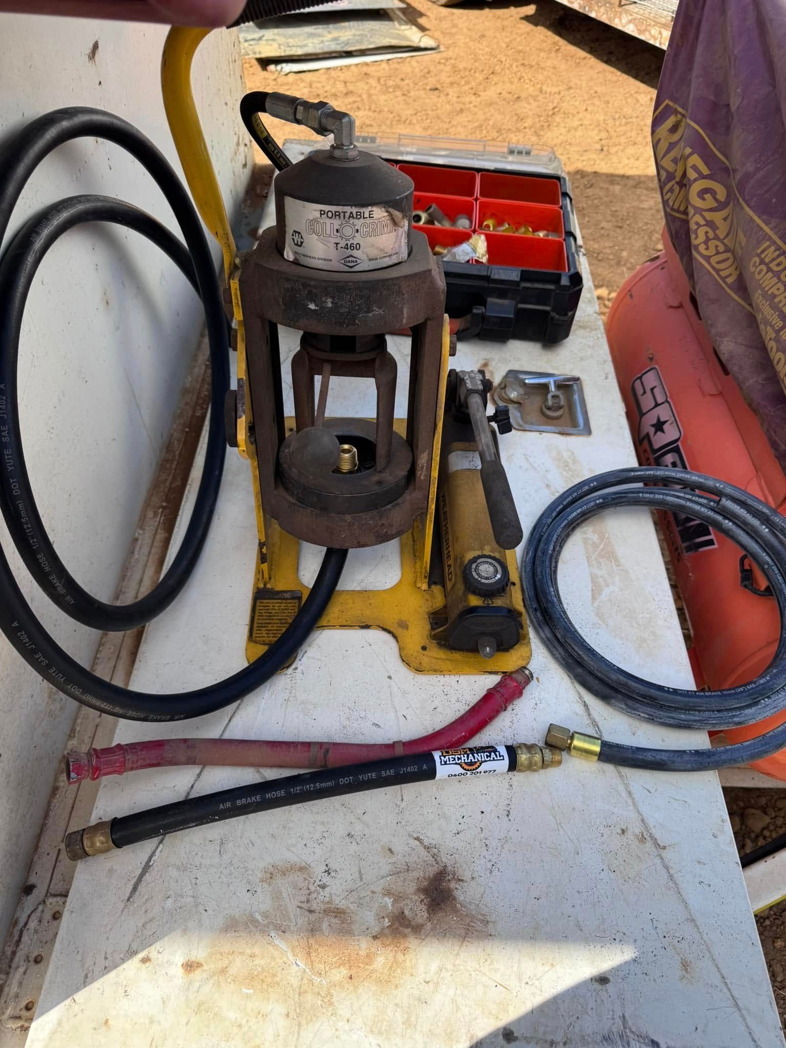Yellow hydraulic hose crimper machine with hoses and fittings on a white surface.