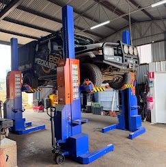 Field with trailer, truck, and red Manitou tracked loader under a bright sun.