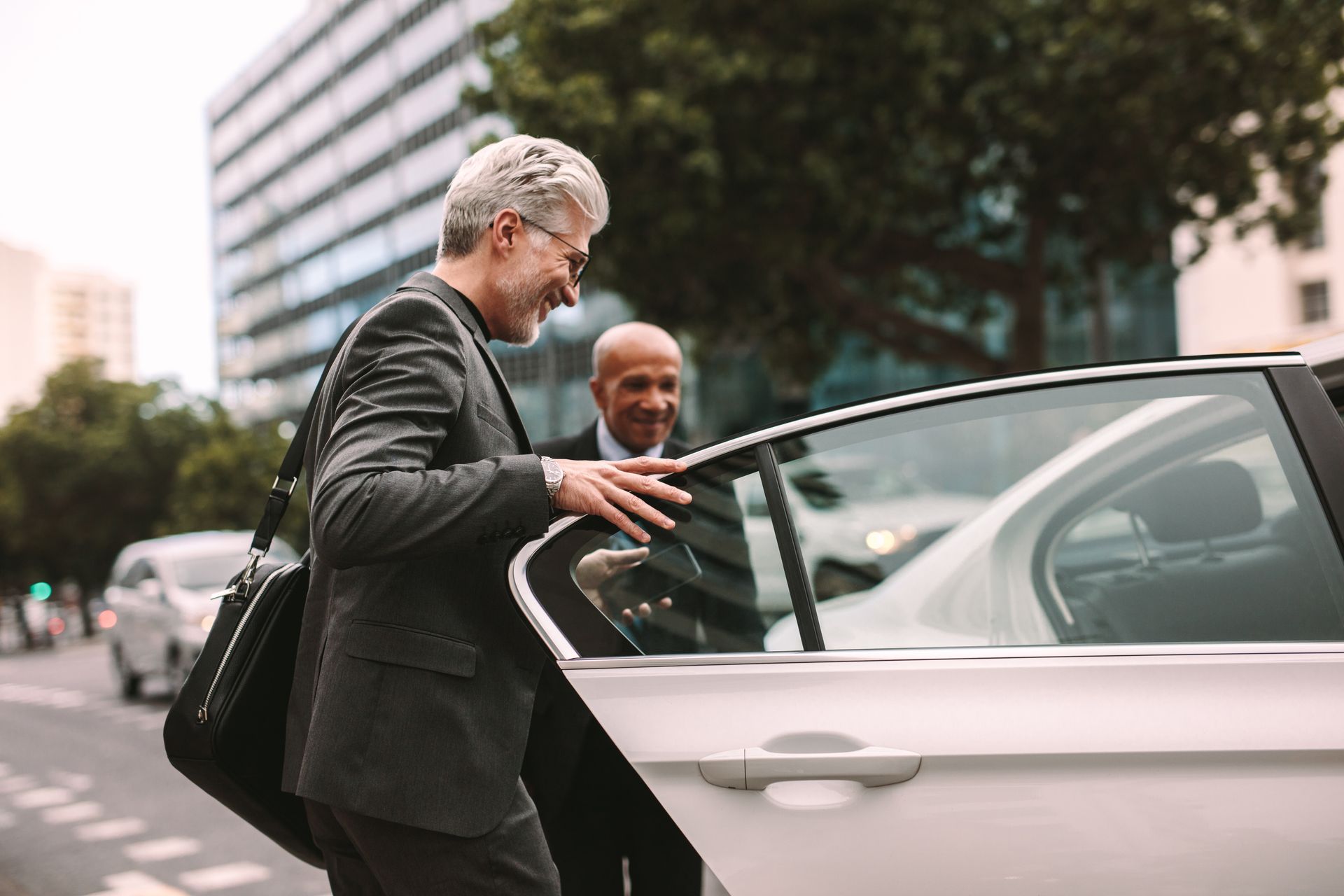 Two people getting out of a silver car on a city street.