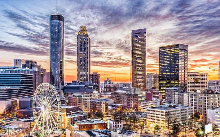 An aerial view of a city skyline at sunset with a ferris wheel in the foreground.