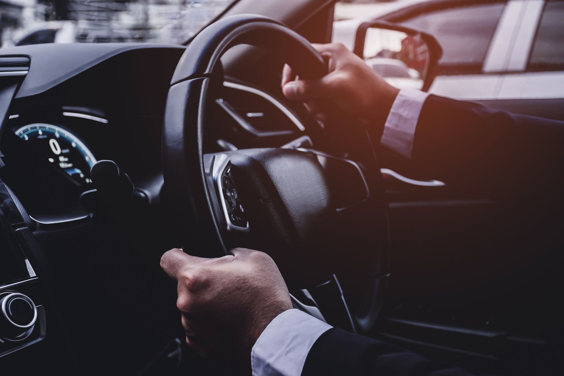 A man in a suit is driving a car and holding the steering wheel.