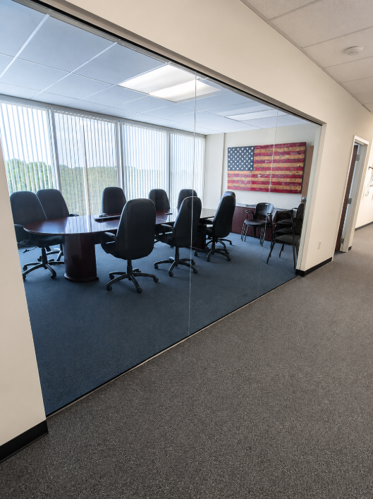 Empty conference room with black chairs around a table, large windows, and an American flag wall hanging.