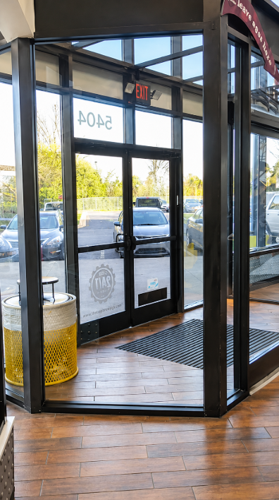 Glass entrance doors with black framing opening to a parking lot, viewed from inside a lobby with wood floor.