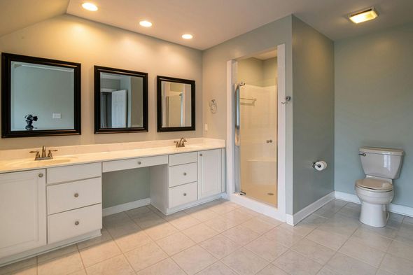 Spacious bathroom with double vanity, mirrors, shower, and toilet; pale blue walls and white cabinets.
