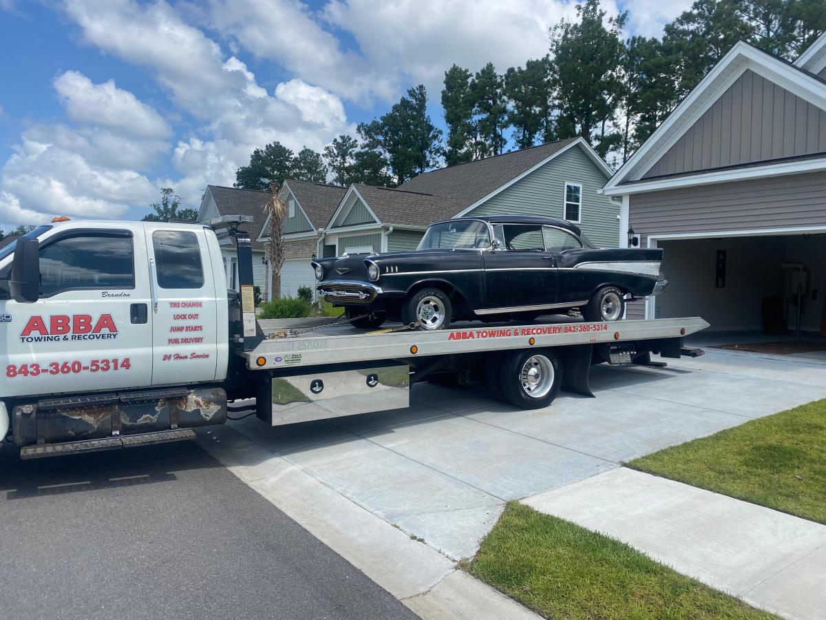 A tow truck with a black car on the back is parked in front of a house.