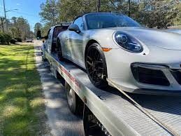 A white porsche 911 carrera gts is being towed by a tow truck.