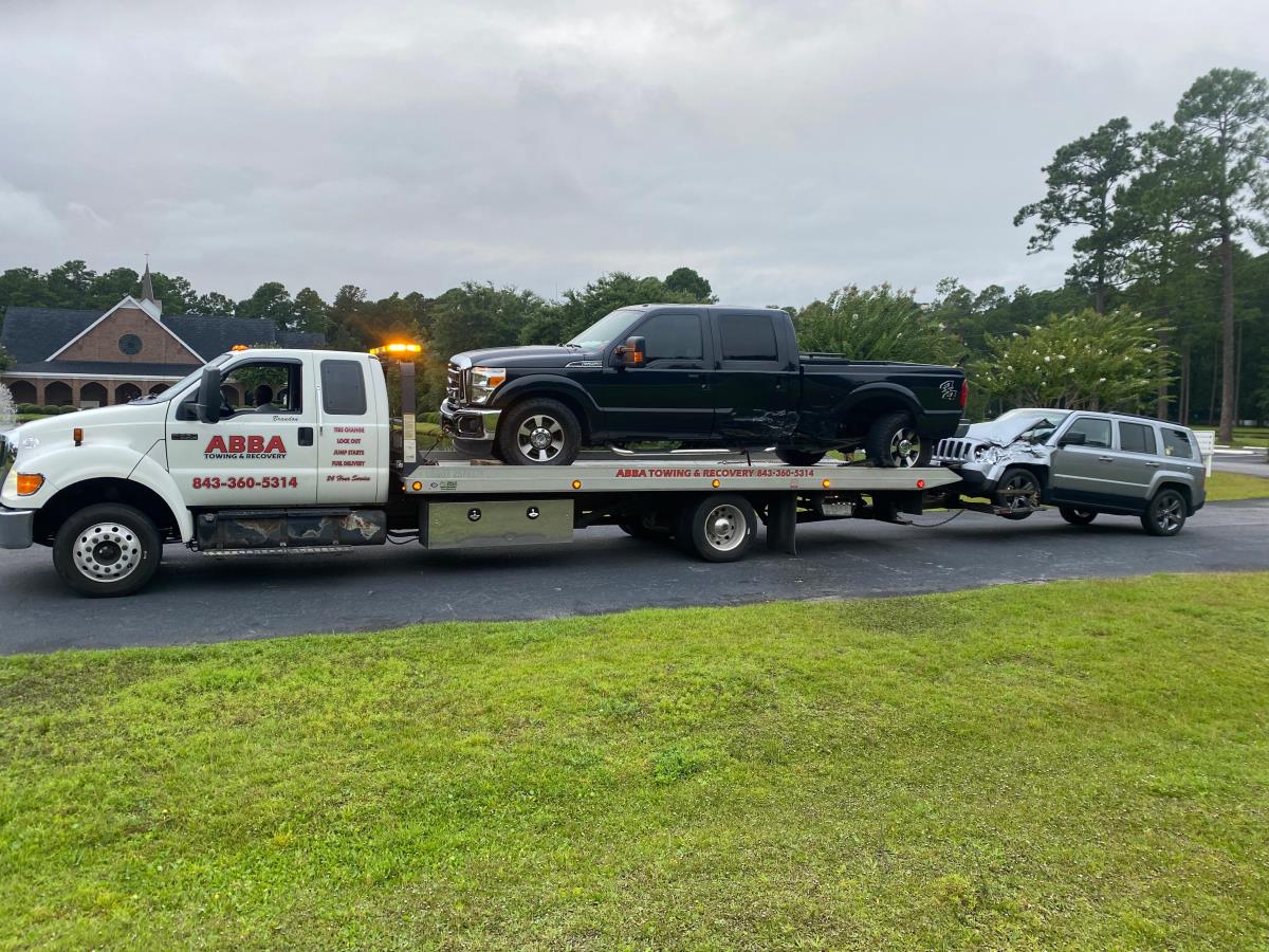 A tow truck is towing a black truck and a silver truck.