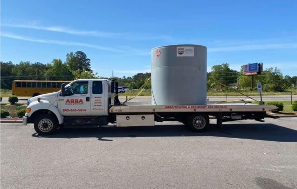 A tow truck with a large cylinder on the back is parked in a parking lot.