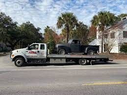 A tow truck is carrying a black truck on a flatbed trailer.