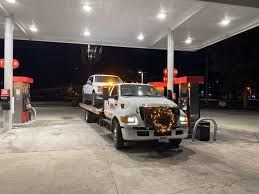 A tow truck is towing a car in a gas station at night.