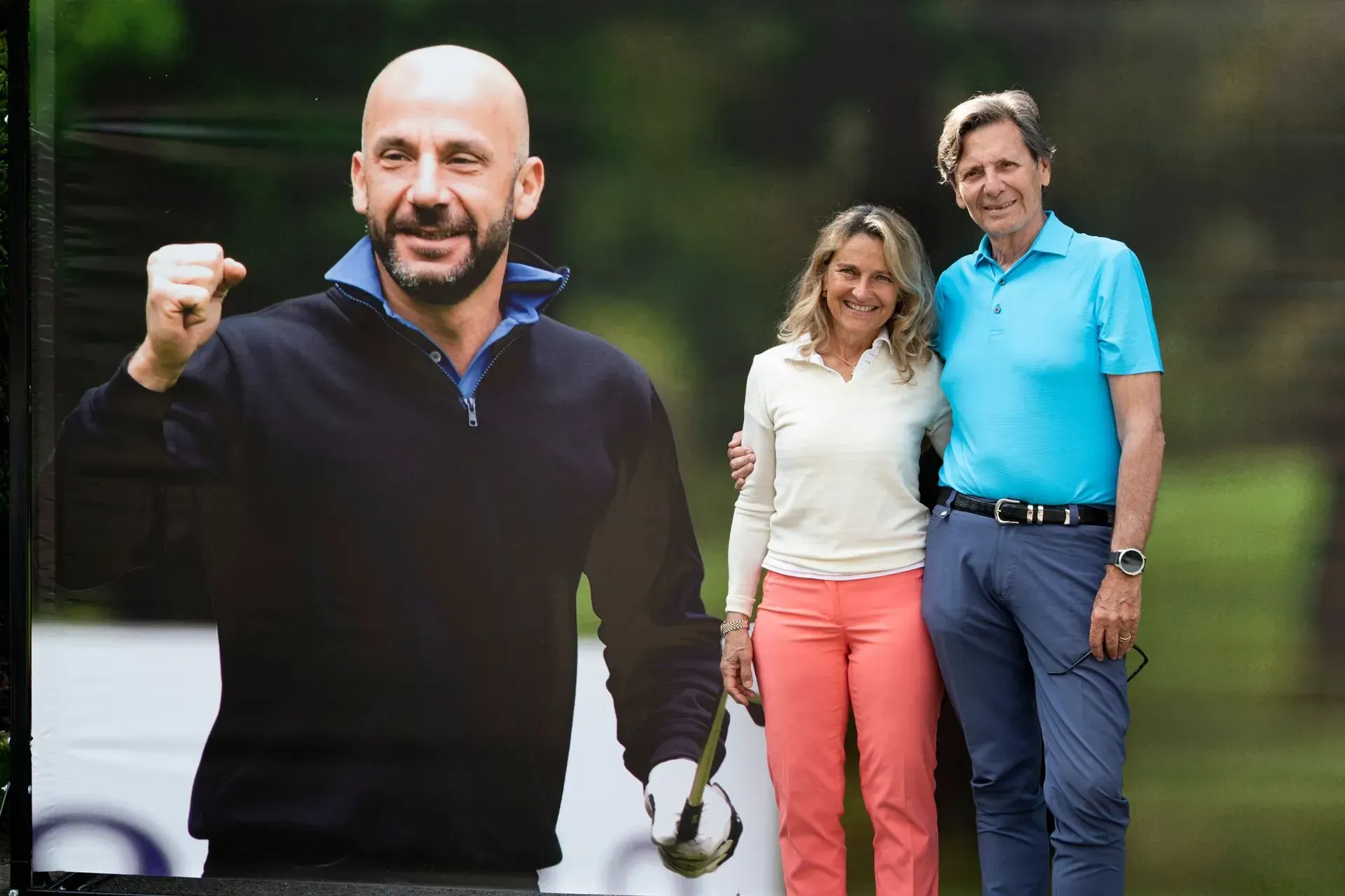 Uomo con il pugno alzato in una foto di un'azione di golf. Una coppia posa con lui, all'aperto in uno spazio verde.