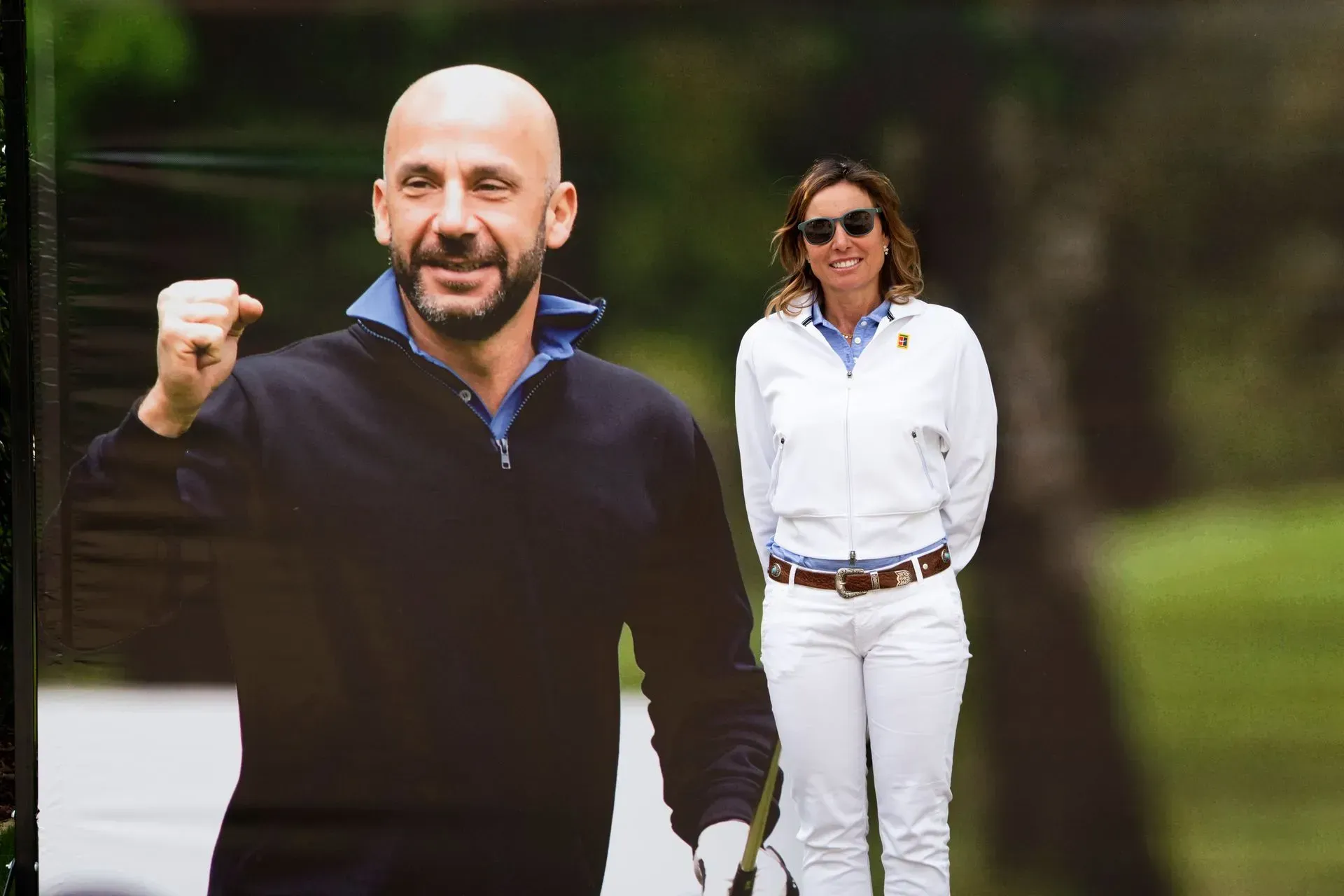 Un uomo con il pugno alzato, accanto a una donna su un campo da golf; entrambi sorridono e indossano abiti sportivi.