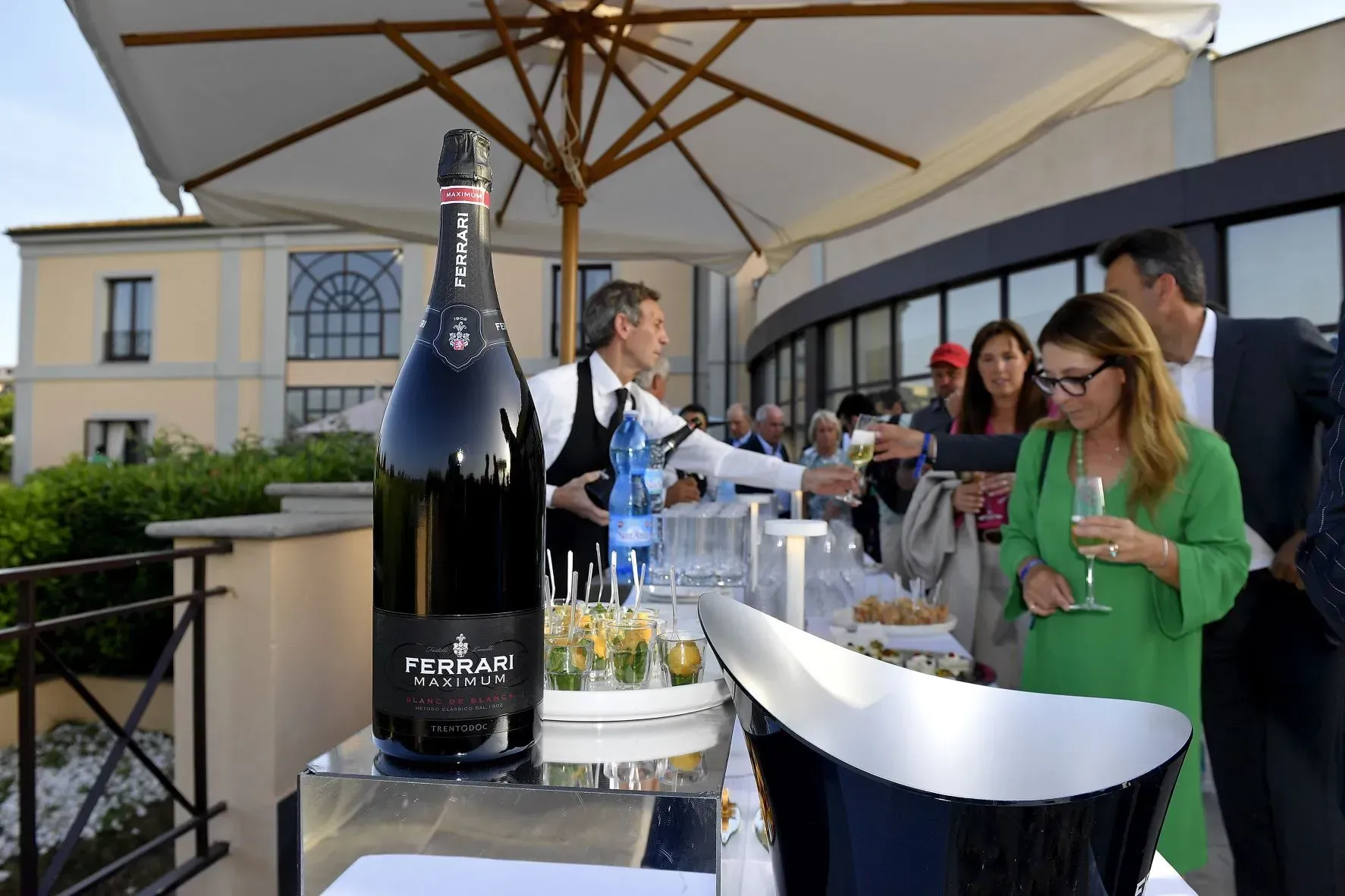 Un cameriere versa champagne durante un evento all'aperto con ospiti su una terrazza.