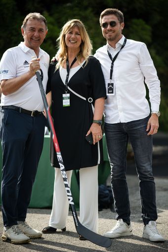 Tre persone posano con una mazza da hockey all'aperto. La donna al centro indossa un abito bianco e nero.