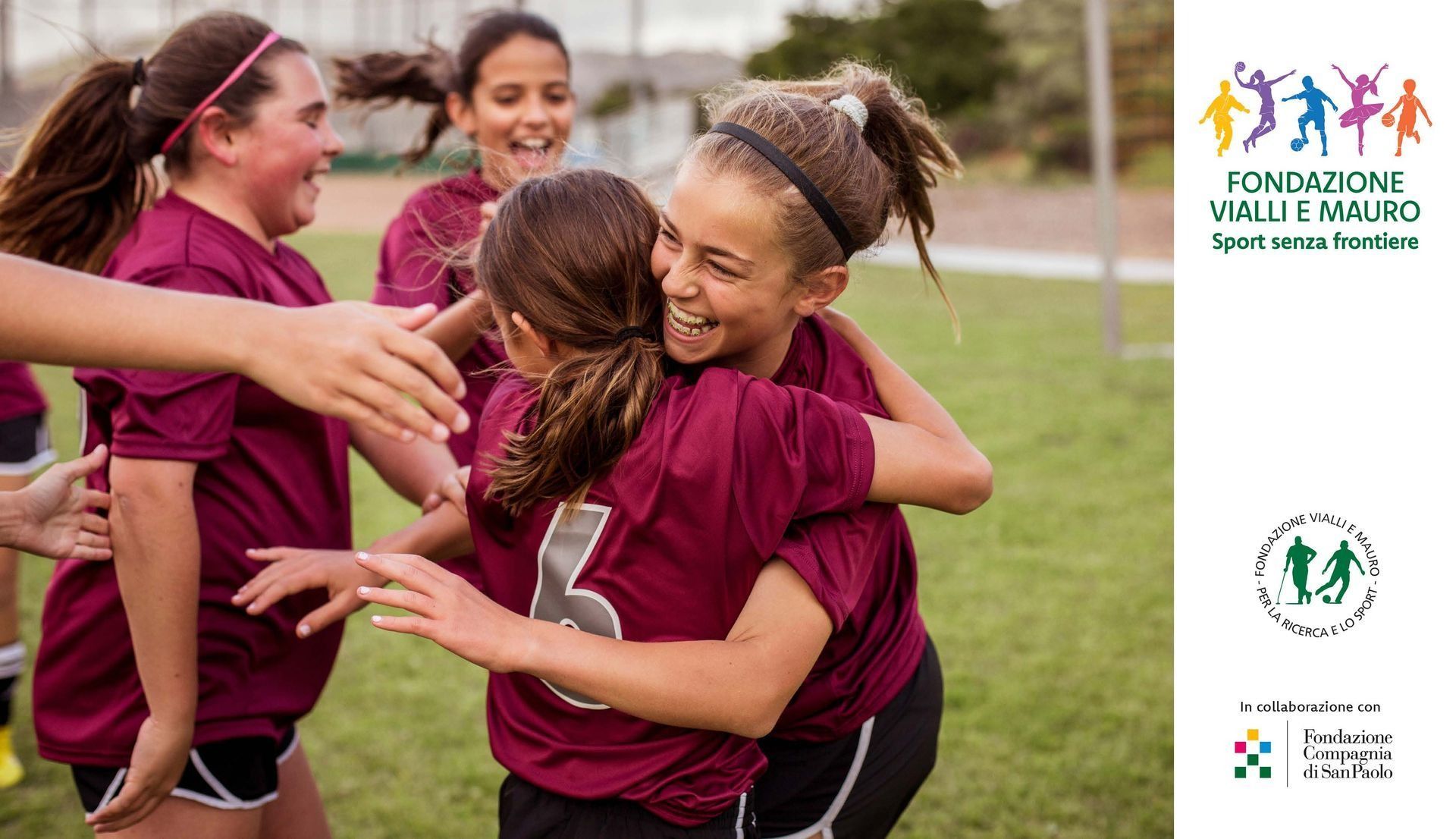 Una squadra di calcio di ragazze festeggia su un campo, indossando maglie color castagna e abbracciandosi.