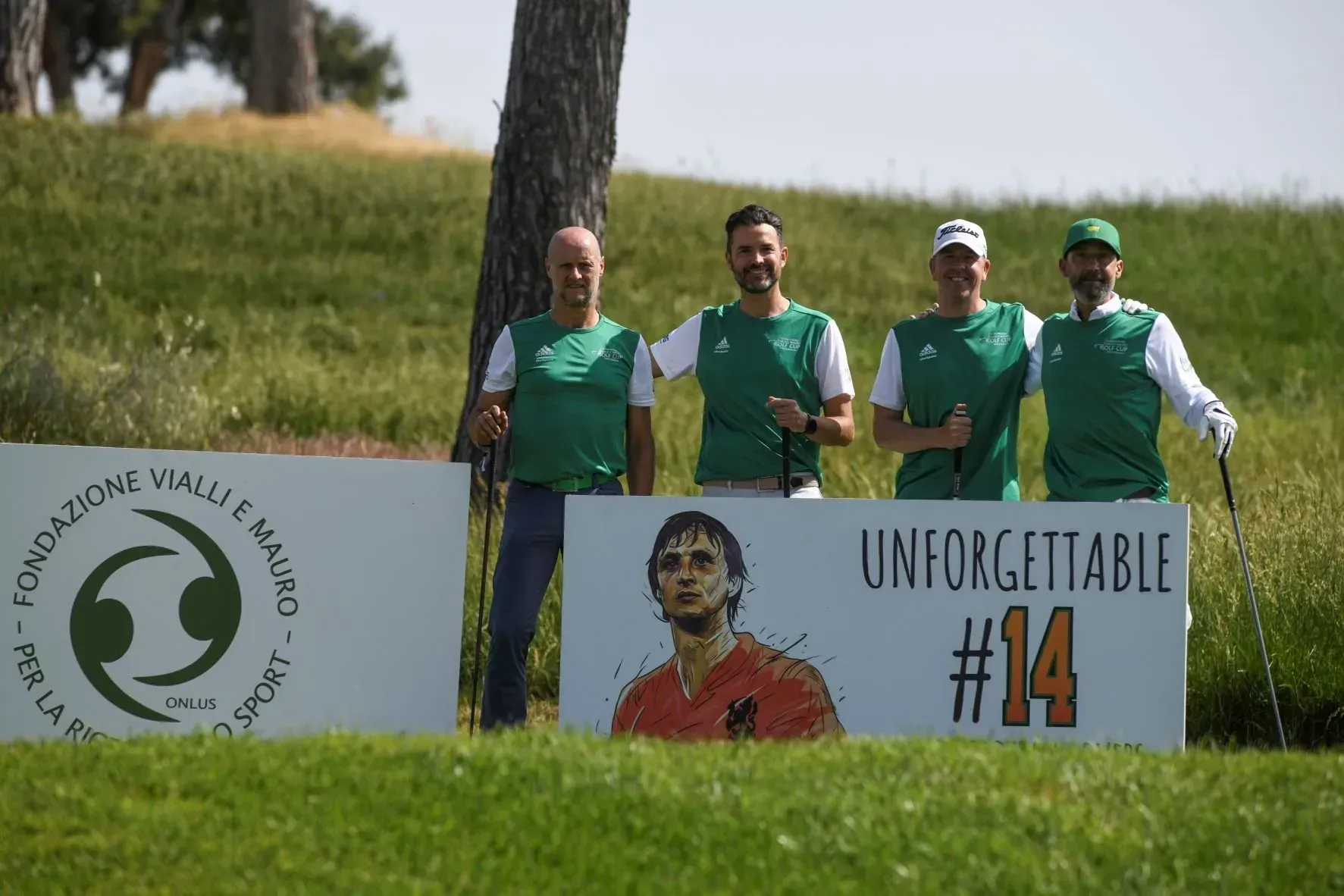 Quattro uomini con indosso gilet verdi tengono in mano delle mazze da golf accanto a un cartello con il ritratto di un calciatore e la scritta "Indimenticabile".