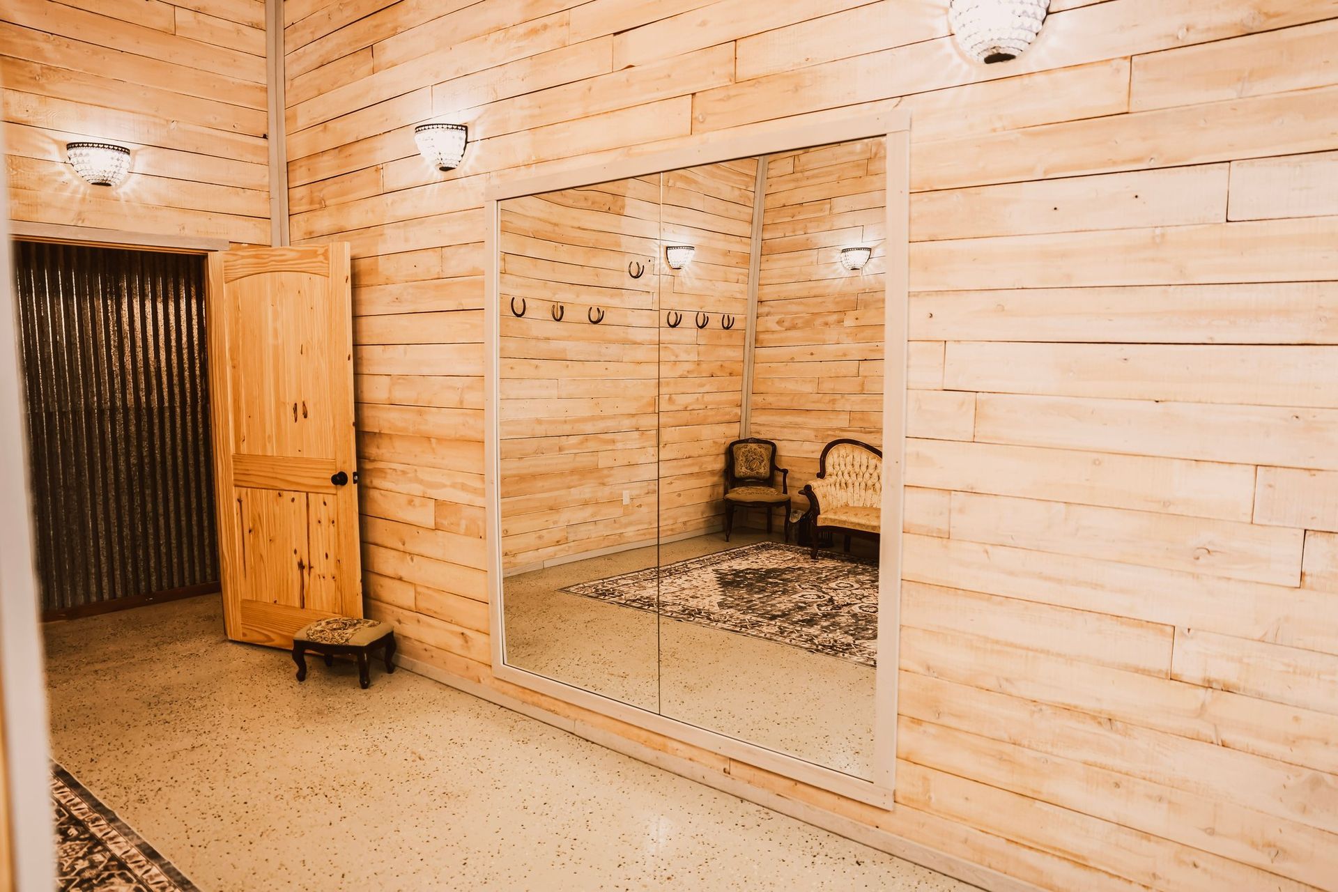 Wooden dressing room with large mirror, door, and seating area reflected.