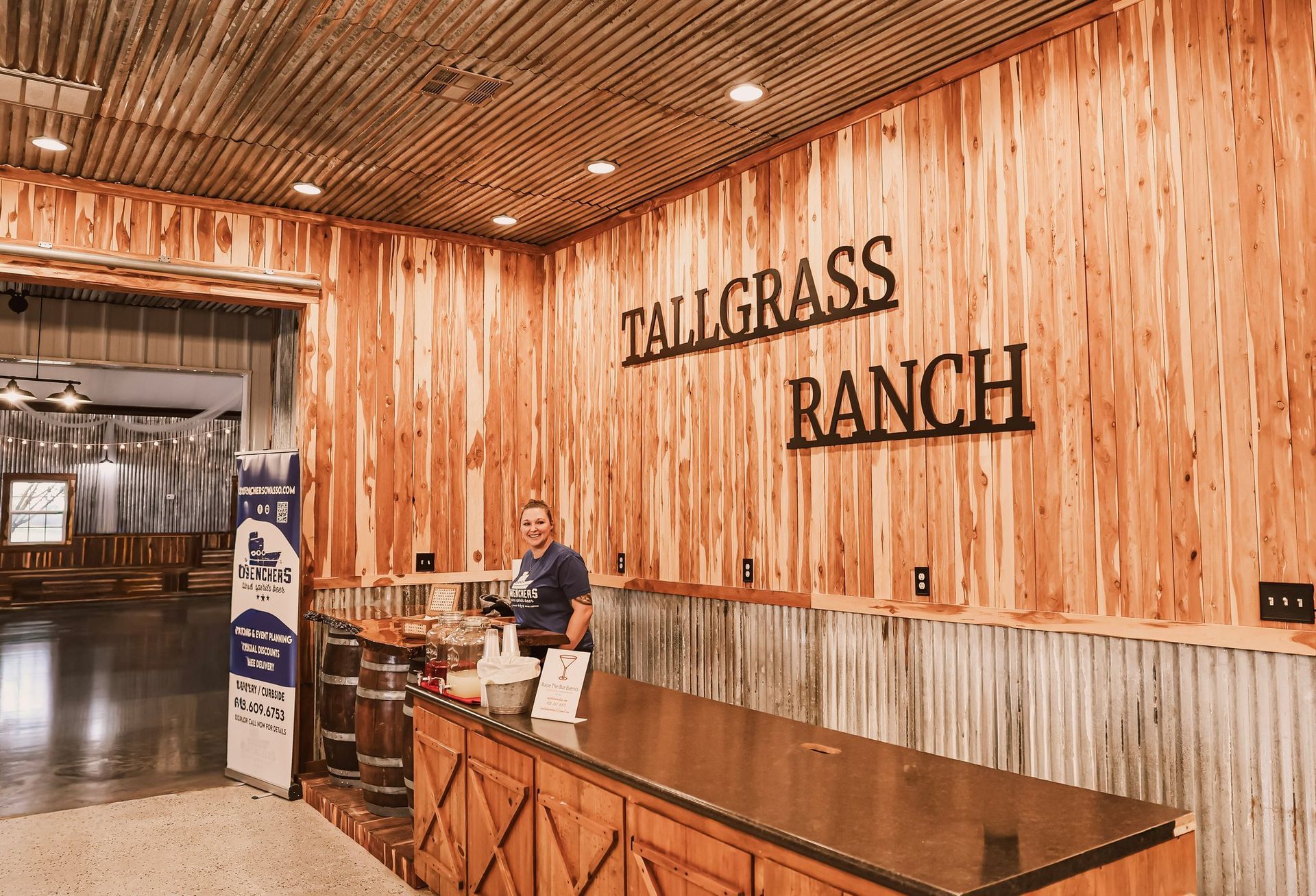 A person stands behind a counter at Tallgrass Ranch, with wooden walls and sign.