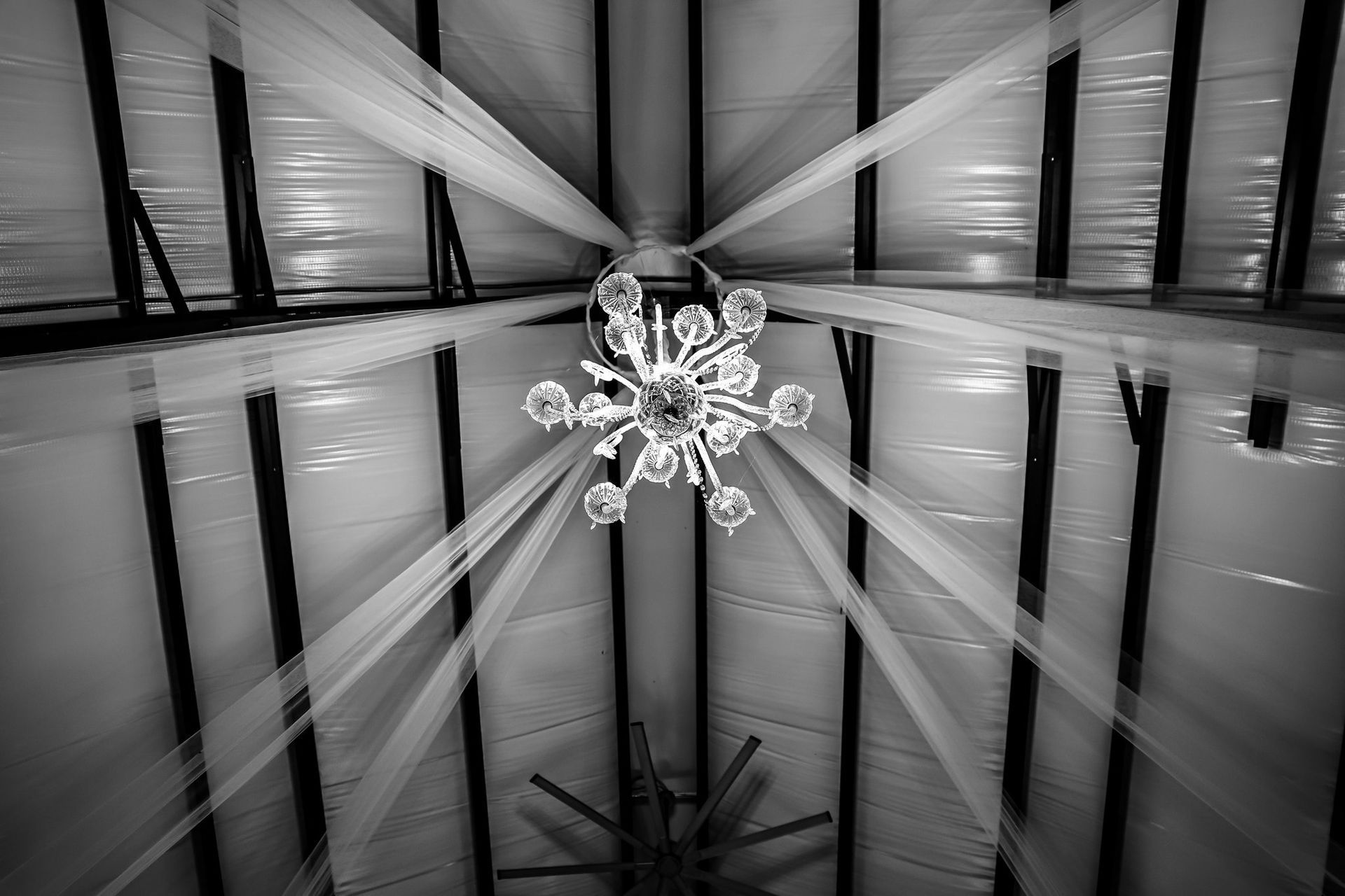 Black and white ceiling with draping fabric and a chandelier, viewed from below.