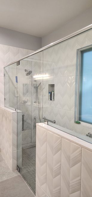 A modern bathroom shower featuring glass walls, light-colored chevron-patterned tile, and chrome fixtures.
