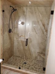A modern walk-in shower with large beige marble-look wall tiles, a mosaic tile floor, and a glass door with black hardware.